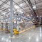 Large, organized warehouse interior with tall metal shelving units filled with boxed inventory, wide polished concrete aisles, overhead industrial lighting, and clearly marked storage locations.